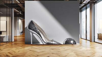 A glamorous silver high heel shoe rests beside a shiny sphere, both highlighted by contrasting light and shadows in an elegant display Wall mural