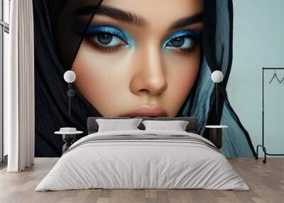 A model exhibits striking blue eye makeup and a black hijab, highlighting contemporary beauty and fashion trends with a serene expression Wall mural