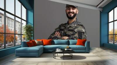 A young man in military uniform stands with arms crossed in front of a gray background. He smiles confidently at the camera Wall mural