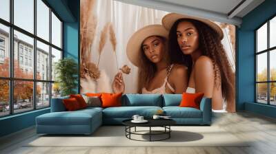 two beautiful african women sitting next to each other, wearing hat, in stylish boho interior. summe Wall mural