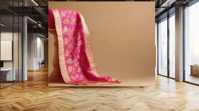 A traditional Banarasi sari in bright pink and gold, draped on a plain wooden stand, simple beige backdrop. Wall mural