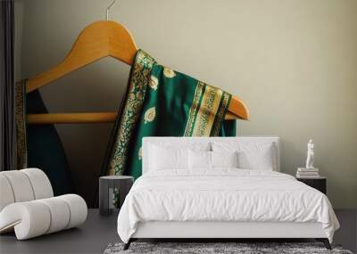 A traditional green and gold sari, elegantly draped on a wooden hanger, set against a clean beige backdrop. Wall mural