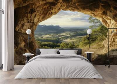 A cave with a natural stone archway, framing a view of the surrounding landscape. Wall mural