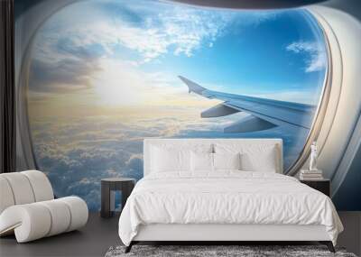 An airplane window showing a breathtaking view of clouds and blue sky, with the wing in the frame. Wall mural