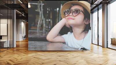 Asian child girl wearing sunglasses and a hat Pose hands chin Wall mural