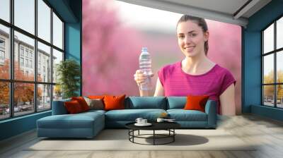 Happy sportswoman holding water bottle looking at you Wall mural