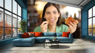 Happy woman eating burger and fries in a coffee shop Wall mural