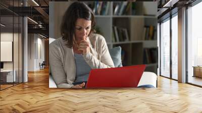 Serious adult woman watching video on laptop at night at home Wall mural