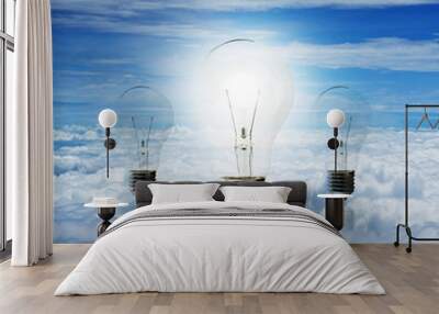 clear electric light bulb glowing against blue sky and cloud bac Wall mural