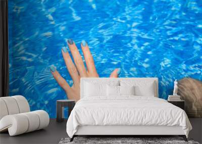 Close-up of female manicured hands. Woman's hands with bright glitter blue fingernails inside of bright blue swimming pool water. Wall mural