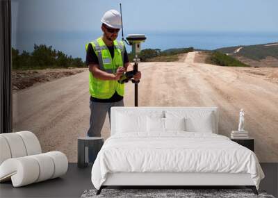 Geodetic engineer surveyor in white hard hat doing measurements with GNSS satellite receiver Wall mural