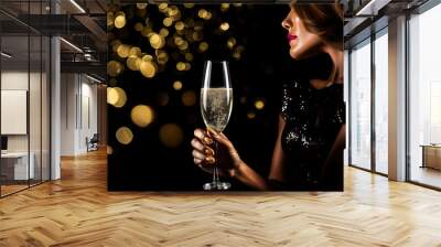 Woman holding glass of champagne on blurred bokeh background. Christmas and New Year celebration concept Wall mural