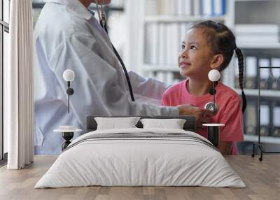 A female doctor uses a stethoscope to listen to the heart rate of a young patient coming to treat influenza which is an epidemic for health care purposes. Medical and healthcare concept. Wall mural