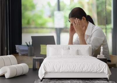 Tired Asian woman working with tax documents on laptop computer in office. Sad, worried, depressed or stressed employee life. Stretch your muscles due to sitting and working for a long time. Wall mural