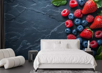 Assorted fresh berries including strawberries, raspberries, and blueberries on a dark stone background with green leaves. Wall mural