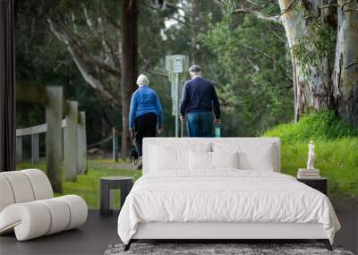 old couple walking with a little dog on a path in a park by the forest. elderly couple in love in australia in spring Wall mural