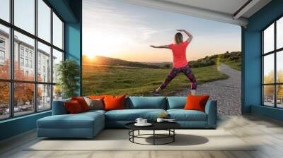 Back view, young woman doing Tai Chi in nature at sunset  Wall mural