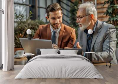 Two younger and elder business professionals discussing project tasks, working on startup plan, development strategy, watching content at laptop, moving hands at screen for explaining ideas. Wall mural