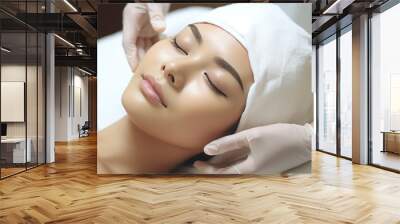 A Beauty expert massaging young woman's face Close up of beautiful Asian woman's head in white hat and doctor's hands in gloves lying on treatment bed. Wall mural