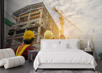 Construction worker and engineer wearing safety gear looking for blueprints in high rise building construction site with tower crane. Wall mural