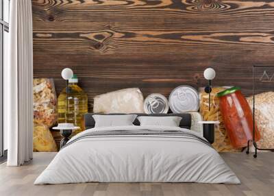 Food donations such as pasta, rice, oil, peanut butter, canned food, jam and other on brown wooden table, top view with copy space Wall mural