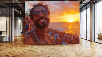 A man takes a selfie with his phone at a music festival, smiling and wearing sunglasses, with a crowd in the background and the golden hour light.  Wall mural