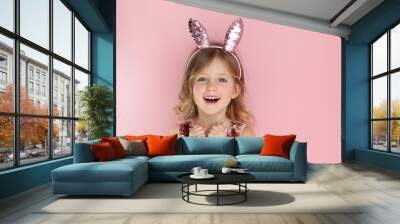 Cute little child wearing bunny ears on Easter day on pink background. Easter girl portrait, funny emotions, surprise. Copyspace for text. Wall mural