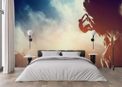 A silhouette of man climbing on rock, mountain at sunset. Wall mural