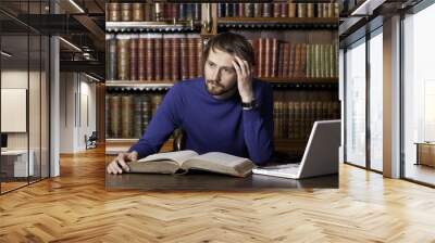 A young man over a book with laptop in classic library Wall mural