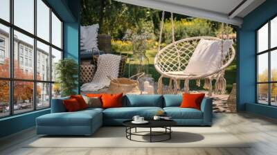 A beige string swing with a pillow on a patio. Wicker baskets, a rug and a blanket on a wooden deck in the garden. Wall mural