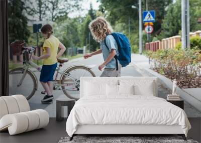 Boy on a skateboard and a girl with a bicycle cross the street Wall mural