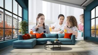 Children during snack time in their classroom. Bottles of fruit and vegetable juices on the desks. White walls. Wall mural