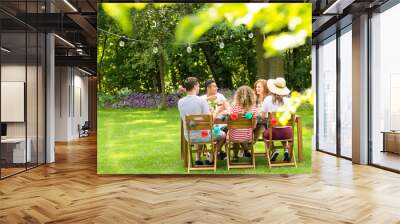 Close-up of blurred leaves in the garden with a group of friends sitting at the table and smiling in the background Wall mural