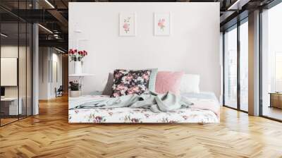 Close-up of flower pattern bed cover and pillows on a bed which is standing against a light color wall with rose illustrations in a feminine classic bedroom interior. Real photo. Wall mural