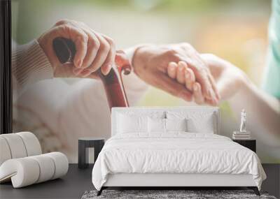 Closeup of senior lady holding walking stick in one hand and holding nurse's hand in the other Wall mural