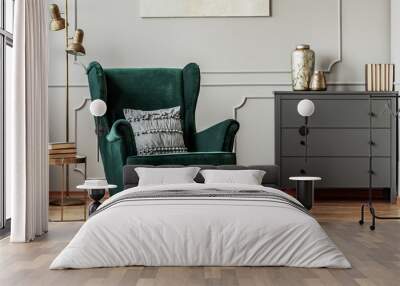 Emerald green wing back chair with pillow in grey living room interior with wooden commode Wall mural