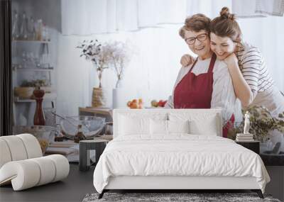 Granddaughter hugging grandmother in the kitchen Wall mural