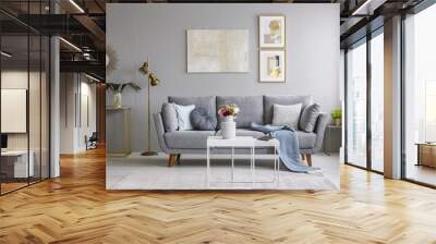 Grey sofa with pillows and blanket standing in bright living room interior with gold lamp, fresh flowers on white table and carpet on the floor Wall mural