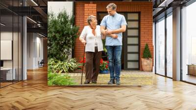 Happy senior lady with walking stick going for a walk with handsome male nurse Wall mural