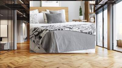 Natural wooden furniture and a cozy, double bed with stylish graphic sheets and pillows in a gray bedroom interior with plants Wall mural