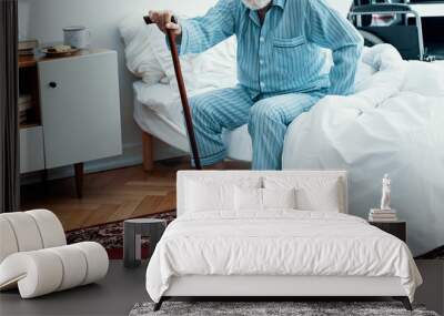 Old sick man with grey beard and hair wearing blue pajamas and sitting on bed at home Wall mural