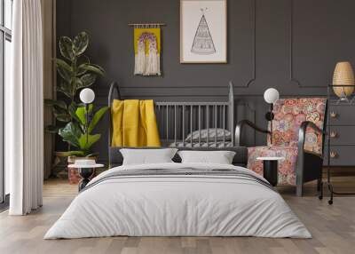 Patterned armchair next to kid's bed with yellow blanket in bedroom interior with plants. Real photo Wall mural