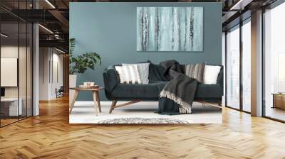 Patterned cushions on sofa next to wooden table and plant in dark apartment interior. Real photo Wall mural