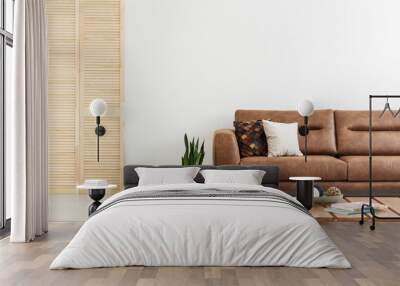 Pillows on brown leather sofa next to plant in white flat interior with wooden screen. Real photo Wall mural