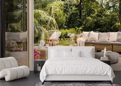 Pouf and rattan sofa on wooden patio with hanging chair in the garden. Real photo Wall mural