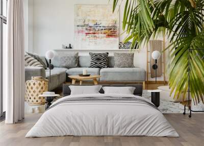 pouf and wooden table in modern living room with painting above grey corner couch. real photo Wall mural