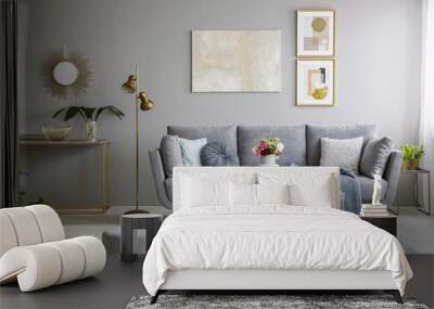 Real photo of a great sofa with cushions and blanket standing in elegant living room interior behind a white table and next to a gold lamp and grey wall with posters Wall mural