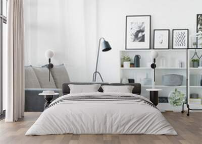 Real photo of a grey couch standing in front of a table that stands on a patterned rug in modern living room interior with shelves with ornaments and posters and a lamp in the bacground Wall mural