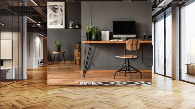 Real photo of an open space interior with black walls and molding. Workspace with desk, chair and computer in the foreground and living room with gray armchair at the back Wall mural