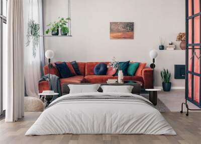 Real photo of colorful pillows on a red corner couch in white living room interior with gray rug Wall mural